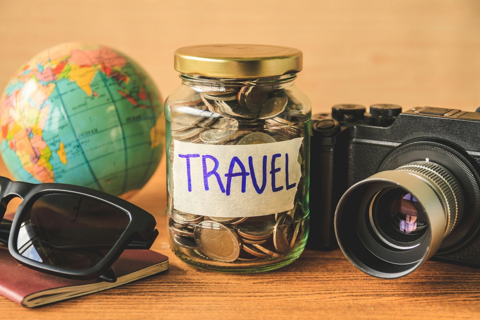 Coins in glass jar with accessories of traveler on wooden table. Saving money for travel concept